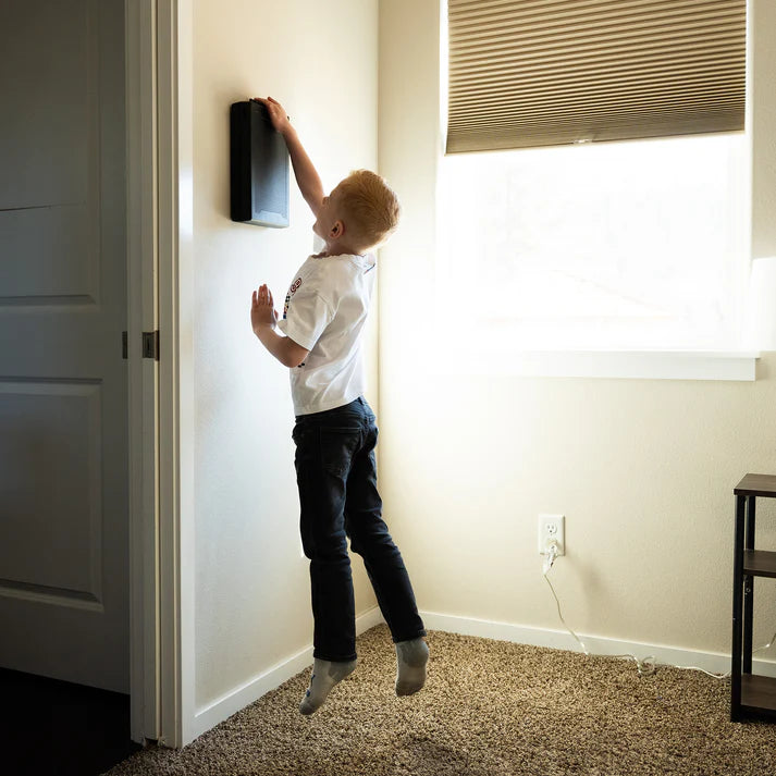 Child interacting with a wall-mounted device in a room with a window and door.