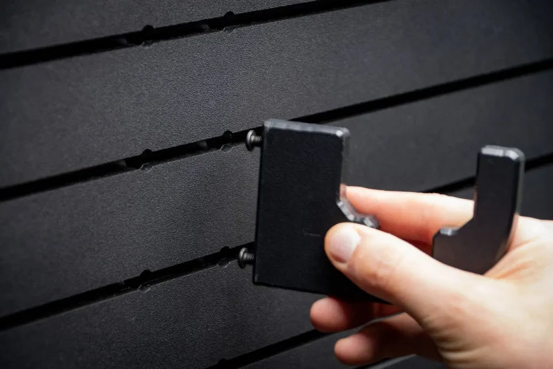 Hand holding a black square object against a dark slat wall.