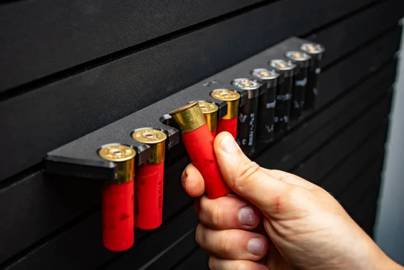 Hand holding red shotgun shells against a black background with shell casings.