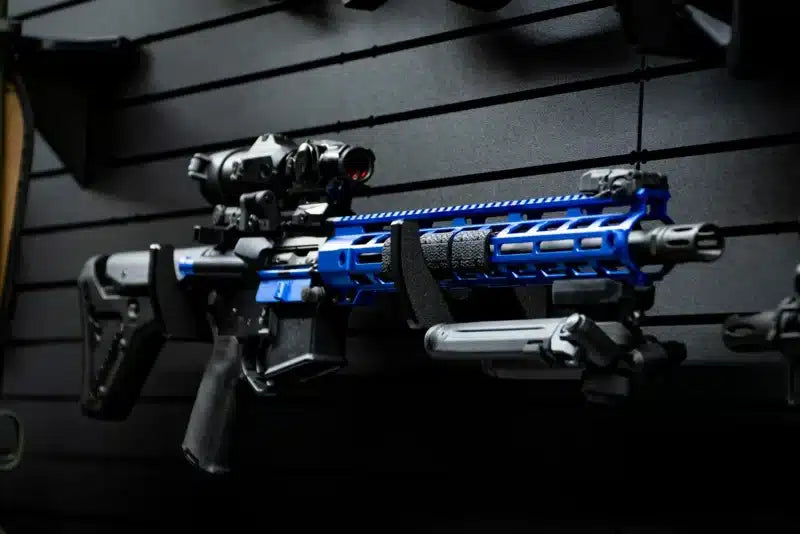 Custom blue-anodized AR-platform rifle with M-LOK handguard, extended magazine, and optic mounted horizontally on a Tactical Walls MWHRACKRS ModWall rack pair, demonstrating how the rack displays custom firearm builds