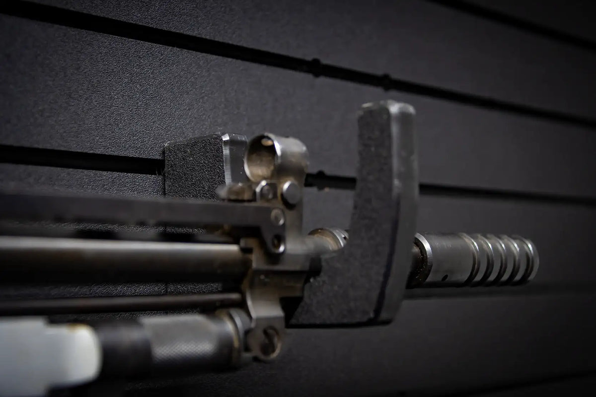 Extreme close-up of a Tactical Walls MWHRACKRS ModWall rack cradling the cylinder and barrel of a stainless revolver-style firearm, showing detail of the black HDPE rack's contoured profile