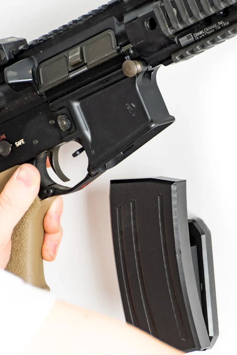 Black rifle with a magazine held by a hand on a white background