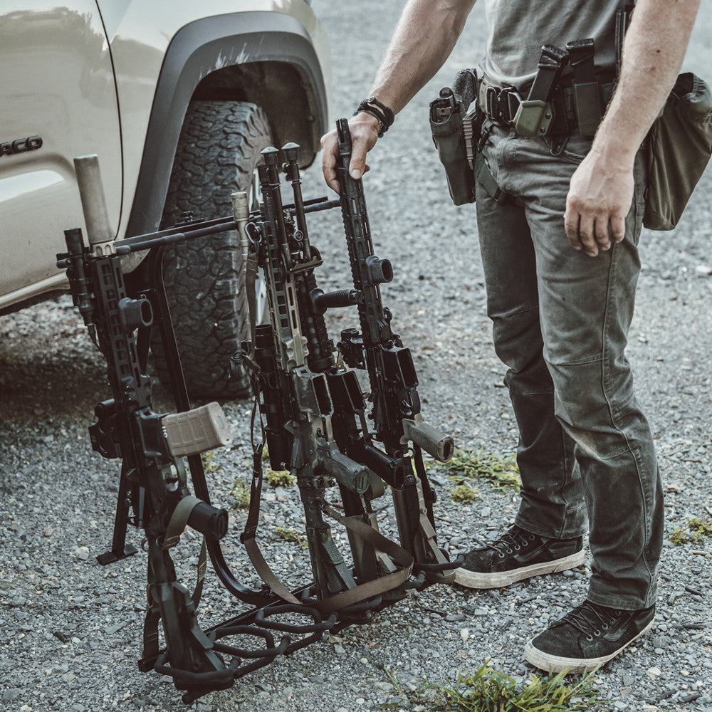 Person holding a tactical rifle rack with multiple rifles in front of a vehicle