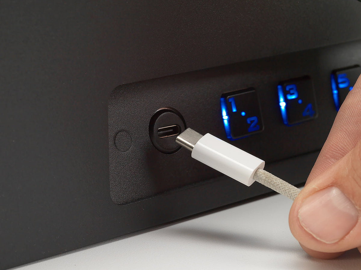 Hand plugging a USB cable into a power strip with multiple outlets and digital displays.