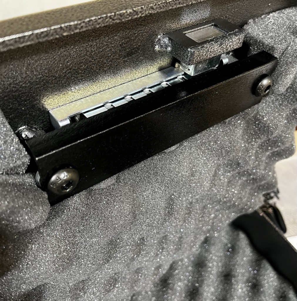 Close-up interior detail of the Fort Knox PB1 pistol box lid underside showing the mechanical Simplex latch mechanism, sliding steel locking bolt, back plate, and hardened mounting hardware that engages the safe body to lock the lid closed