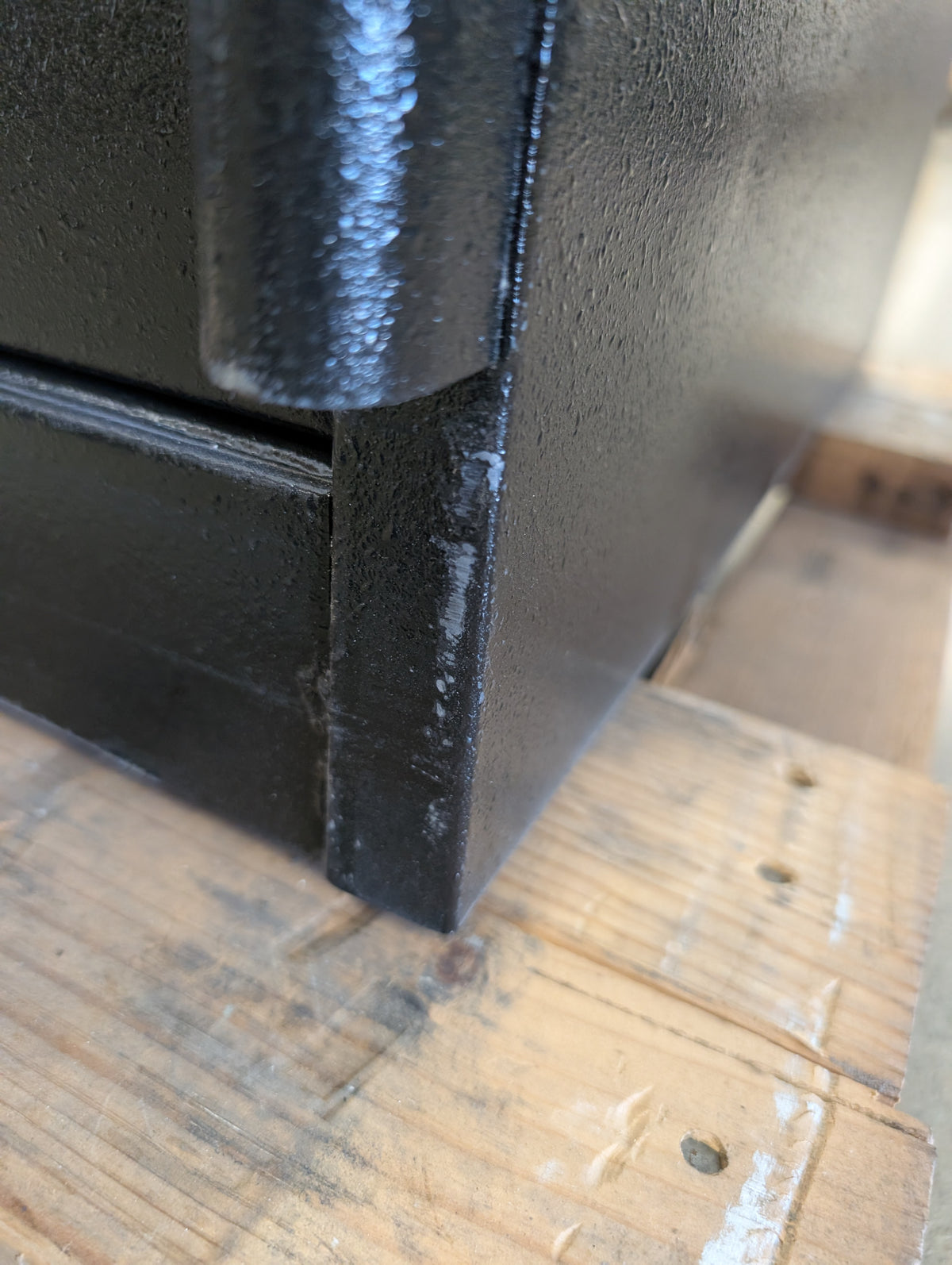 Close-up of the right lower hinge with a scratch and some paint chips on the lower body of the safe. 